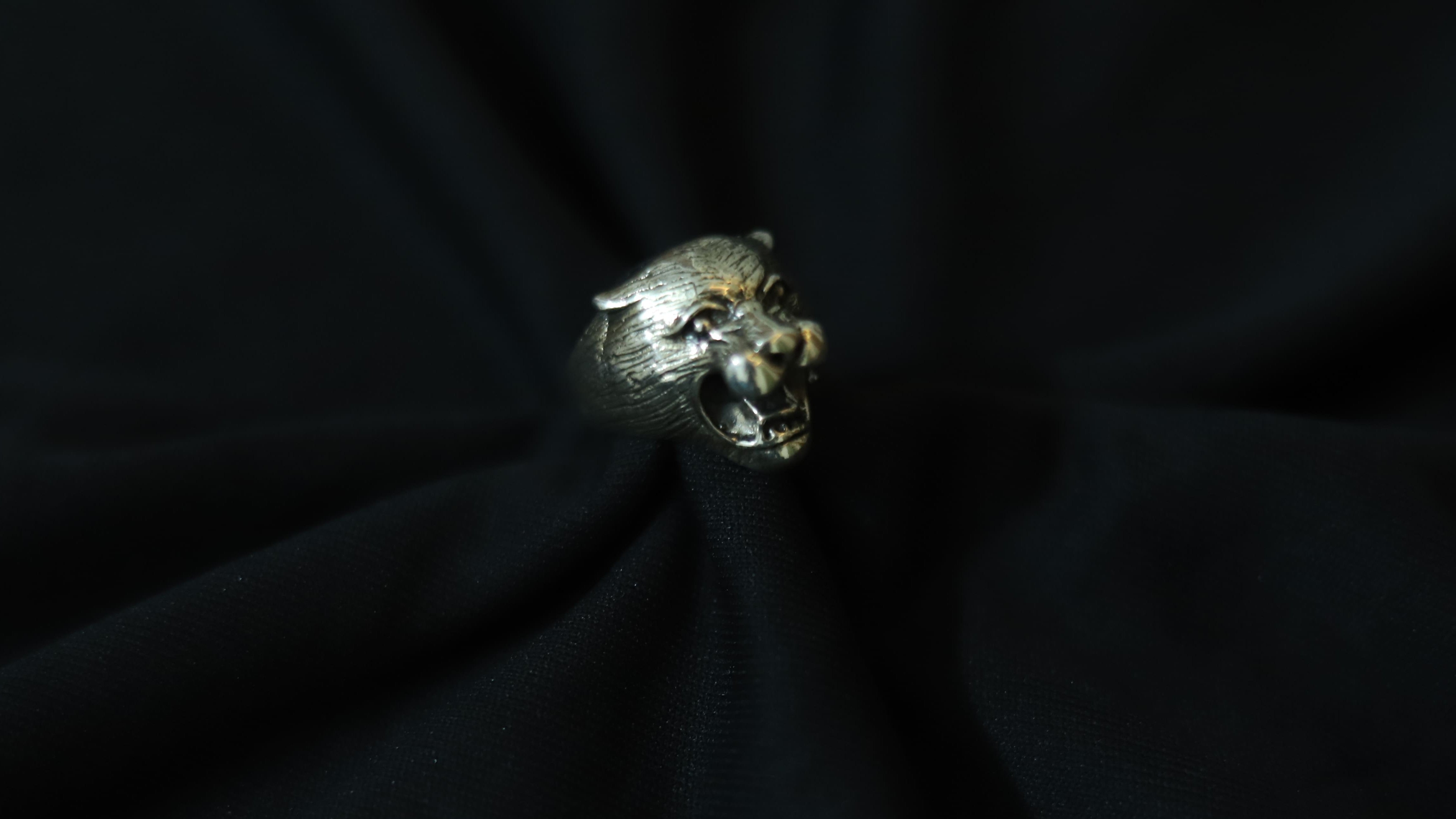 A silver-toned ring shaped like a roaring panther head, displayed on a dark black fabric background.